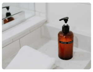 Dispensador de jabón líquido para manos junto a toalla blanca en un lavabo.